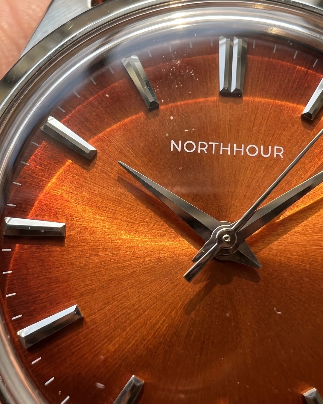 Close-up of a burnt-orange sunburst watch dial with polished steel hands and markers