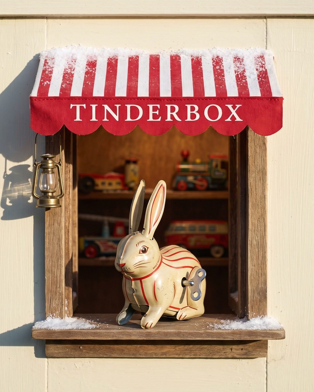 A wind-up tin rabbit sitting in a tiny shop hatch under a red and white striped TINDERBOX awning