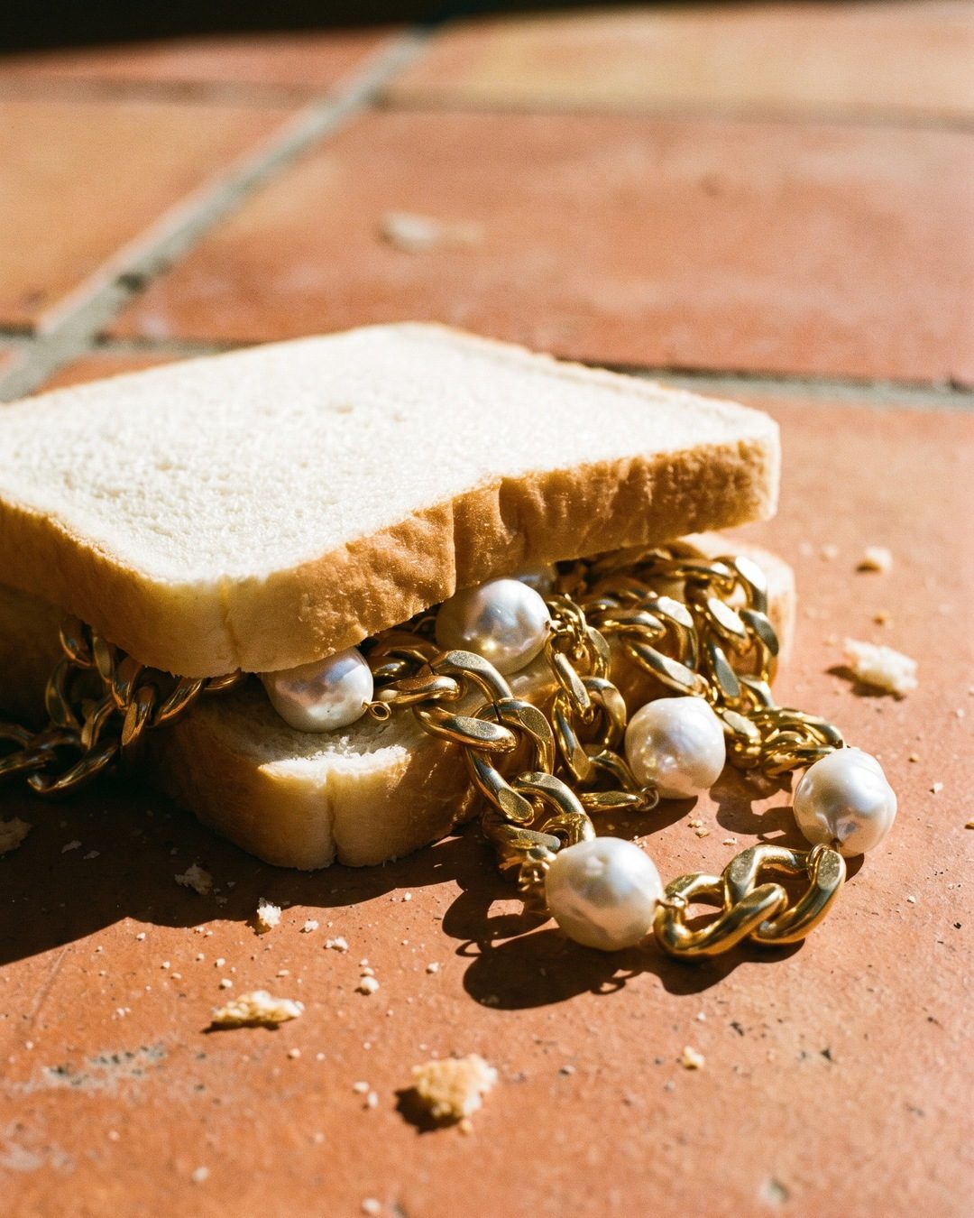 A white-bread sandwich on terracotta tiles with chunky gold chains and baroque pearls spilling out
