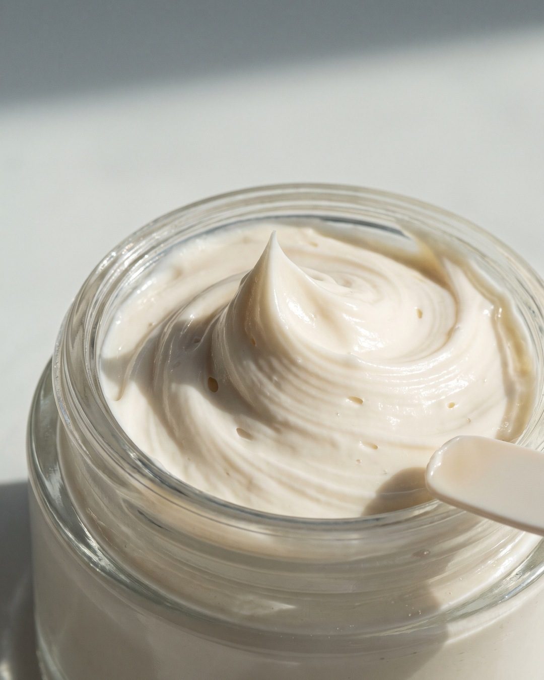 Close-up of a whipped ivory face cream peak in an open glass jar