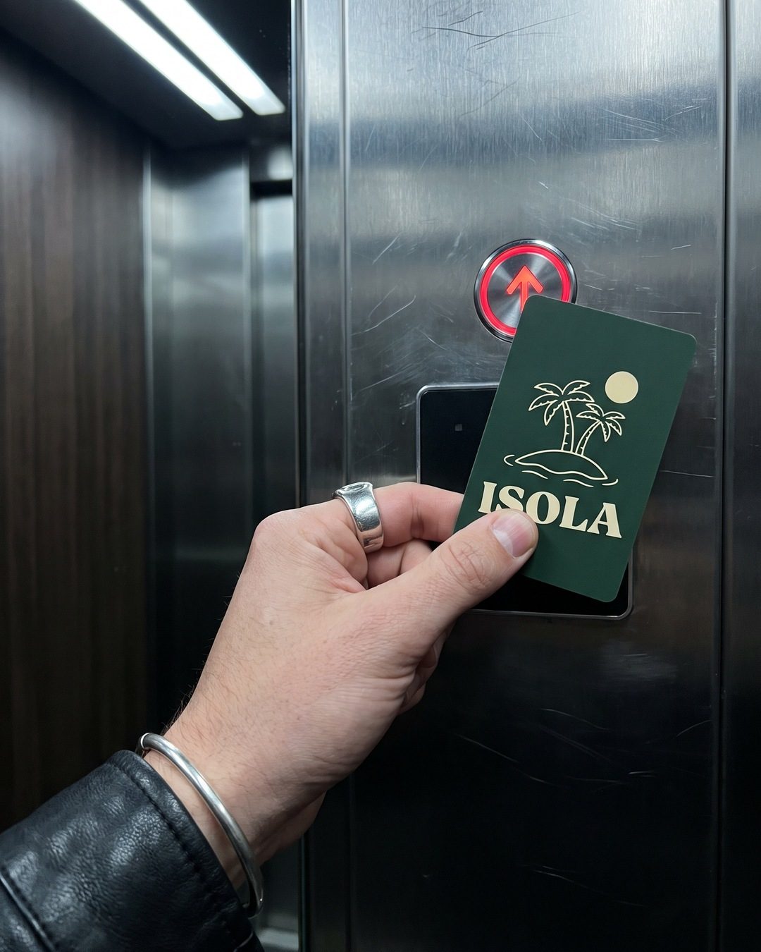 A hand with a silver ring tapping a green Isola key card on a lift card reader