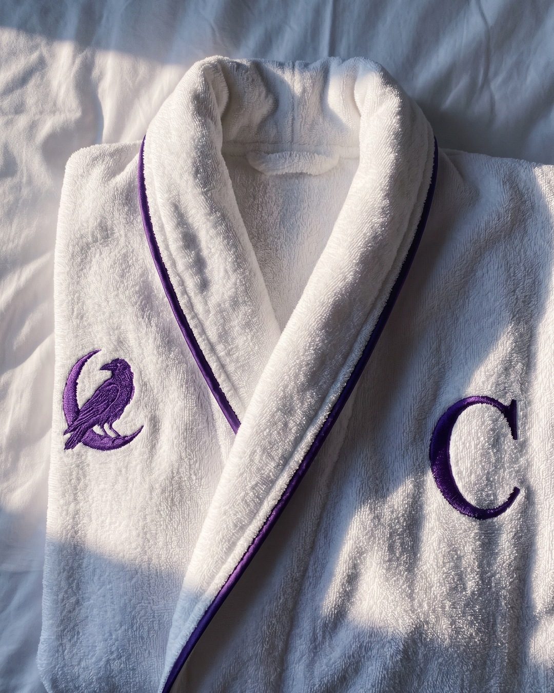 A white robe with violet piping, embroidered with a crow on a moon and a C monogram